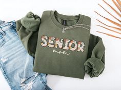 a green shirt with the word senior on it next to ripped jeans and a plant