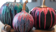 three painted pumpkins sitting on top of a wooden table next to a pine cone