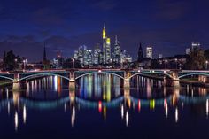 a city skyline is lit up at night with lights reflecting in the water and bridge