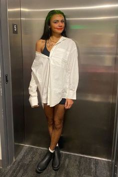 a woman with green hair and black boots standing in front of a metal elevator door