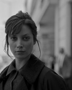 a black and white photo of a woman in a coat looking at the camera while standing outside