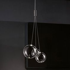 three glass balls suspended from the ceiling in a room with black walls and flooring