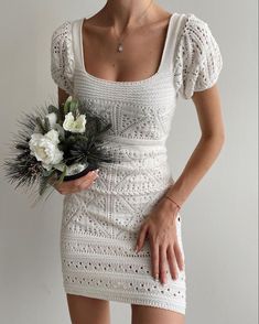 a woman in a short white dress holding a bouquet of flowers and wearing a necklace