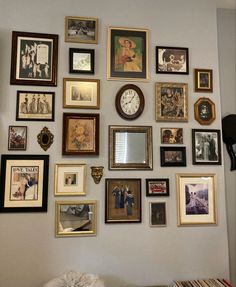 a wall with many different framed pictures on it and a clock mounted to the wall