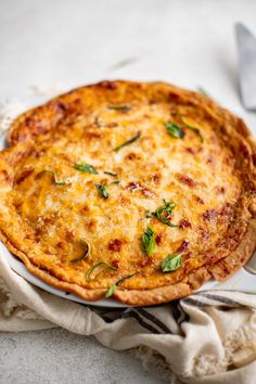 a cheesy quiche on a white plate with a fork and napkin next to it