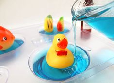 a yellow rubber duck sitting on top of a blue bowl filled with liquid next to other plastic ducks