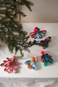 several colorful paper flowers are on a table next to a christmas tree and pine branches