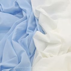 white and light blue sheets are laying together on the bed sheet, as if they were made from silk or polyester