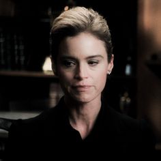 a woman with blonde hair and black shirt in front of bookshelves looking at the camera