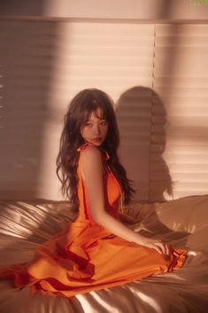 a woman in an orange dress sitting on a bed