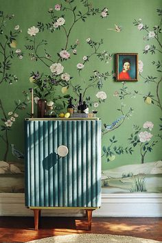 a green room with flowers and paintings on the wall, along with a blue cabinet