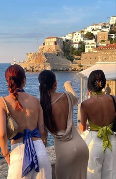 three women standing on the beach looking out at the water