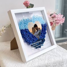 a white frame with blue roses in the shape of a heart and an image of a couple