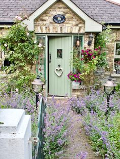 a green door surrounded by lots of flowers in front of a stone building with potted plants