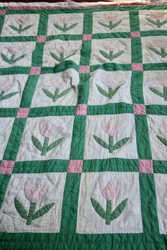 a green and white quilt with pink tulips on the center is laying on a bed