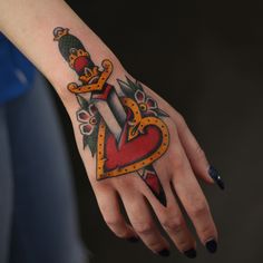 a woman's hand with a heart and dagger tattoo on her left arm,