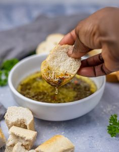 a hand holding a piece of bread over a bowl of pesto and tofu