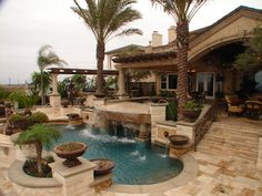 a large pool surrounded by palm trees in front of a house with an outdoor dining area