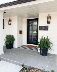 two planters on the front porch of a house with black door numbers and lights