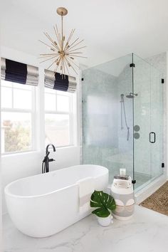 a white bathtub sitting next to a window in a bathroom under a chandelier