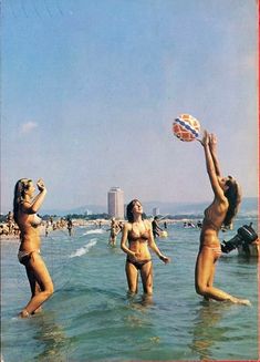 three women in bathing suits playing with a ball on the beach