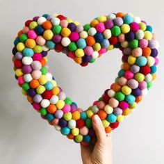 a hand holding up a heart made out of pom - poms