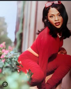 a woman in a red dress and sunglasses sitting on a ledge next to pink flowers