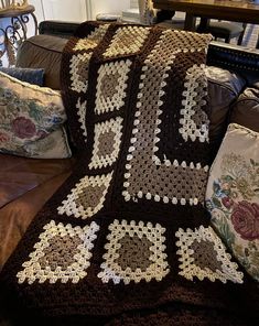 a crocheted blanket is sitting on a couch next to pillows and a table