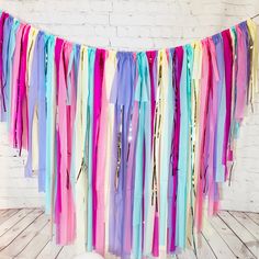 multicolored streamers hanging from the ceiling in front of a white brick wall