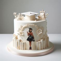 a white cake with a woman in a graduation cap on top