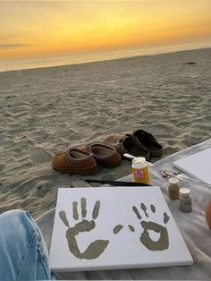 a person sitting on top of a beach next to a white board with a hand and foot print