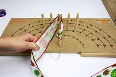 a person is sewing on a piece of fabric with wooden skewers in the background