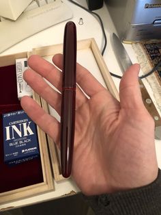 a person holding a pen in their hand next to a box with an ink stamp on it