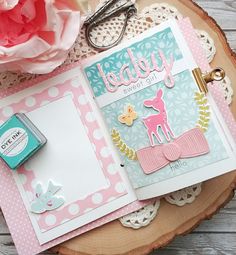 an open scrapbook with paper and scissors on top of a wooden table next to a pink flower