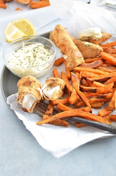 a plate with chicken, fries and dipping sauce on it next to some lemon wedges