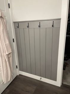 a white coat hanging on the wall next to a door with hooks and towel rack