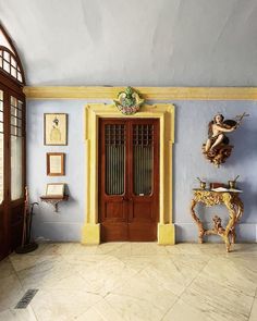 a room with blue walls and yellow trimmings, an ornate table and two wooden doors