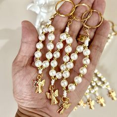 a person holding some gold and white beads with angel charms in their hands on a table