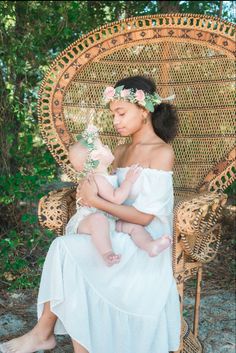 a woman sitting in a wicker chair holding a baby and wearing a flower crown