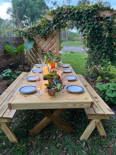 a wooden table with blue plates and place settings on it in the grass next to a fence