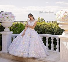 a woman in a wedding dress standing on a balcony with flowers and bushes behind her