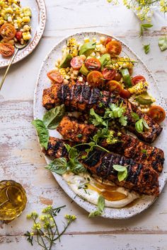 grilled meats and vegetables on a plate next to a glass of olive oil