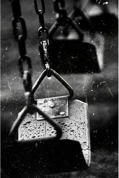 a black and white photo of a swing set with rain drops on the seat area