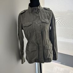 Army (Khaki) Green Utility Jacket From The Gap Dropped Shoulders, Snap-Button Cuffs. Stand Collar, Hidden Front Zip And Snap-Button Closure. Utility Pockets At Chest And Hips Interior Tie-Belt Ties And Cinches At Waist. Stitch Detailing Throughout. "How To Style" Ideas Included Fabric & Care: 97% Cotton, 3% Lycraspandex Machine Wash. Military Style Khaki Utility Jacket With Buttoned Pockets, Spring Military Outerwear With Buttoned Pockets, Khaki Military Utility Jacket With Button Cuffs, Military Style Khaki Utility Jacket With Button Cuffs, Khaki Military Outerwear With Button Closure, Military Style Khaki Outerwear With Button Closure, Military Style Khaki Outerwear For Work, Khaki Button-up Utility Outerwear, Spring Khaki Utility Jacket With Button Cuffs