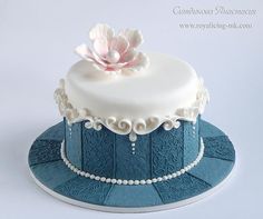 there is a blue and white cake with a flower on top that has pearls around the edges