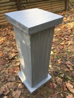 a cement planter sitting in the middle of leaves on the ground next to a fence