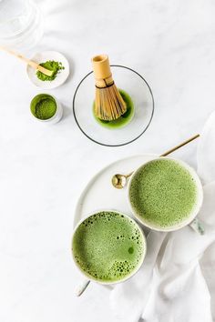 two cups filled with green liquid on top of a white plate