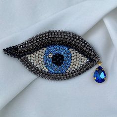 an evil eye brooch with blue and white beads on it's side, next to a tear drop