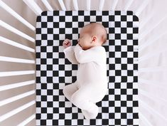 a baby laying on top of a black and white checkered mat next to a wall