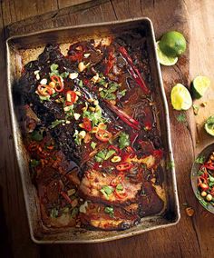 a pan filled with meat and vegetables on top of a wooden table next to sliced limes